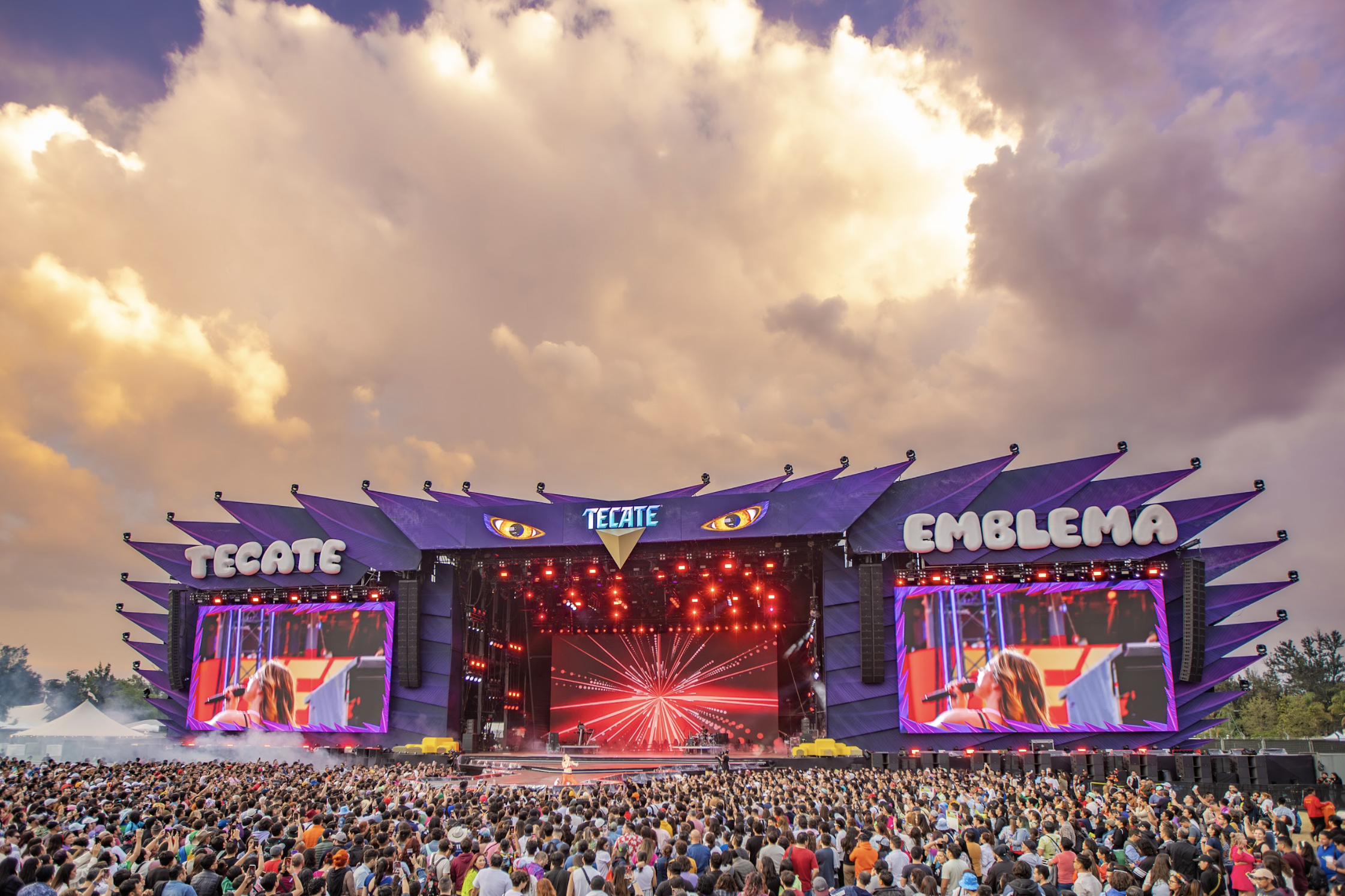 Multitud disfruta de un festival de música con un gran escenario y pantallas que muestran un artista en vivo
