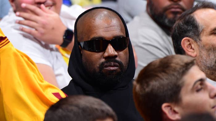 Kanye West wearing sunglasses and a hoodie at a basketball game