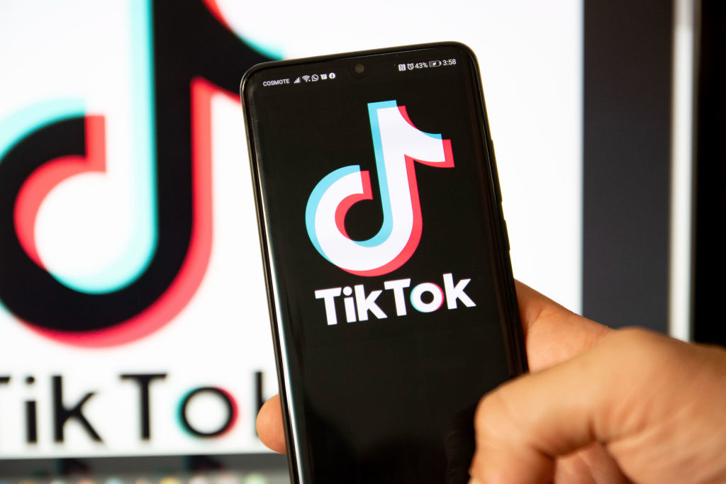 Hand holding smartphone with TikTok logo on screen, TikTok logo also blurred in background