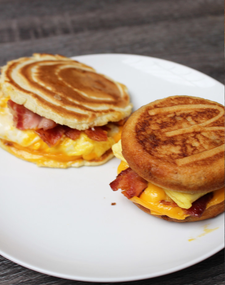 Breakfast sandwich with pancakes, bacon, and melted cheese on a plate