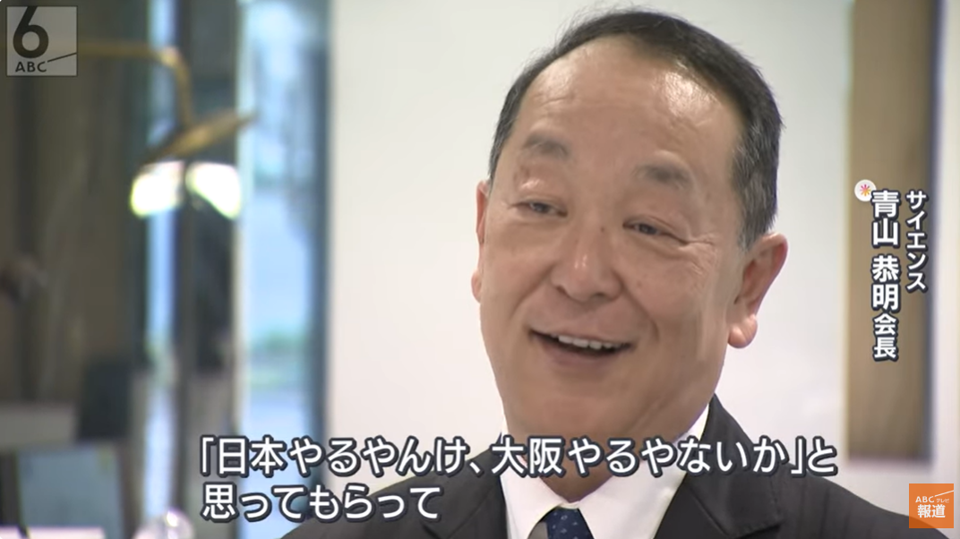 男性がカメラに笑顔で話している、背景にミラーがあります。画像に表示されているテキストは「日本を変えるか、本部を変えないか」というメッセージです。