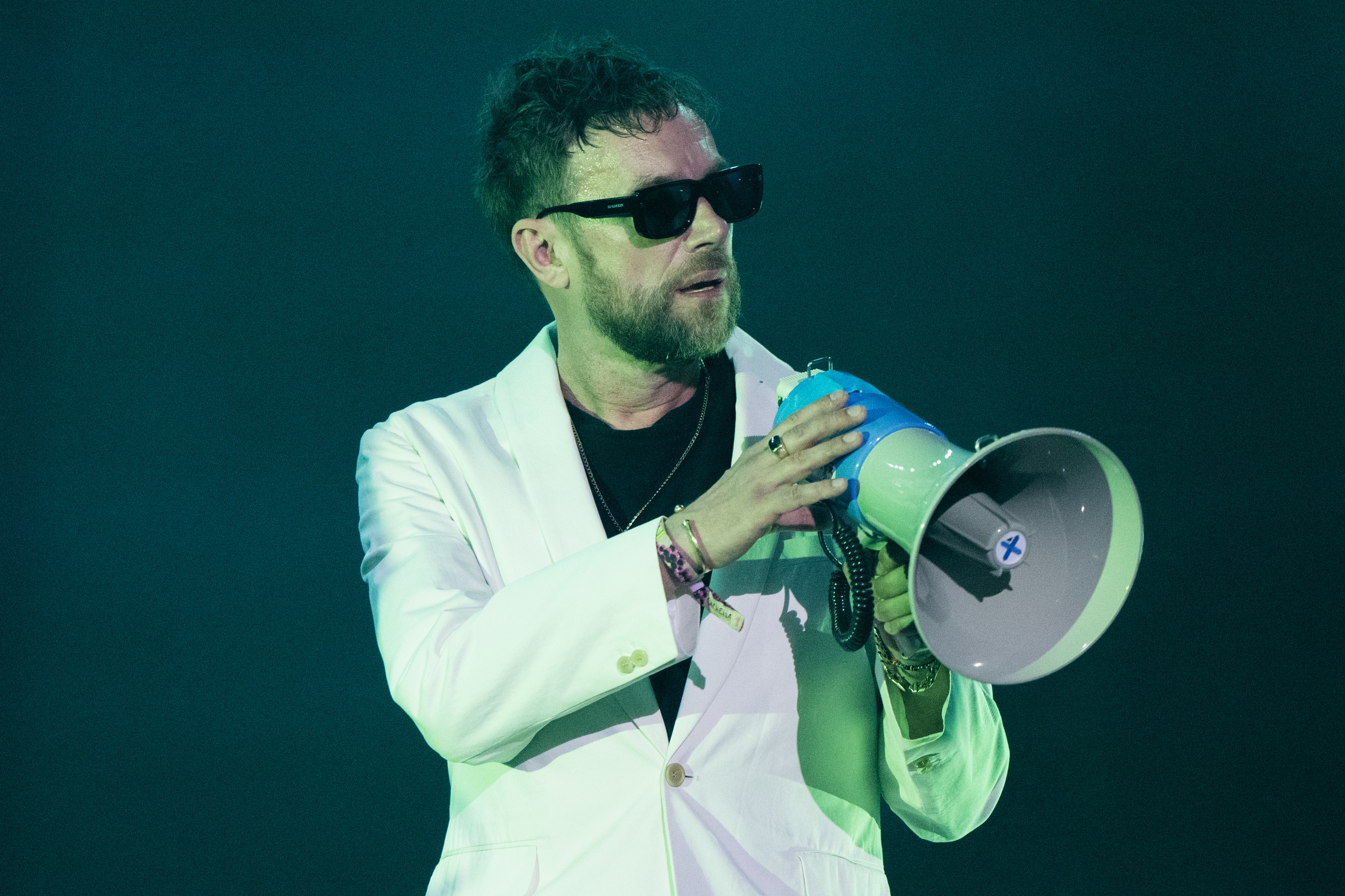 Music artist in a white suit speaks into a megaphone onstage