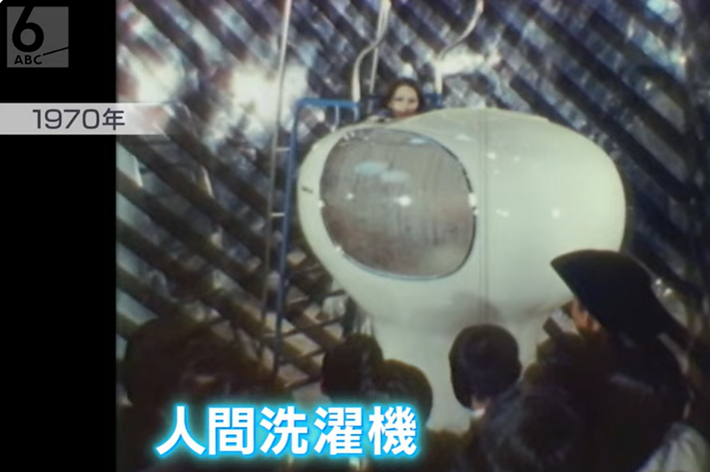 古いテレビ番組の映像で、人々が未来的なヘルメット型装置を見ています。