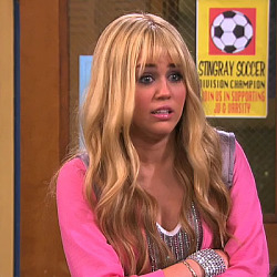 Hannah Montana (Miley Cyrus) looks surprised in a pink top with a long blonde wig
