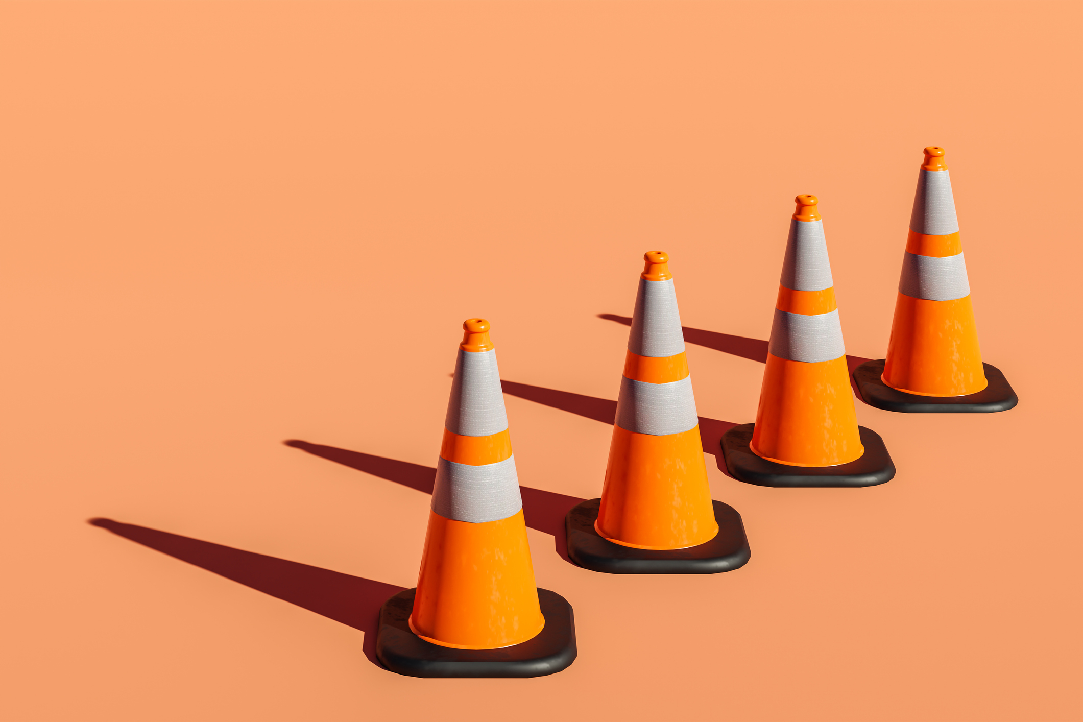 Four traffic cones in a row on a plain surface, casting shadows