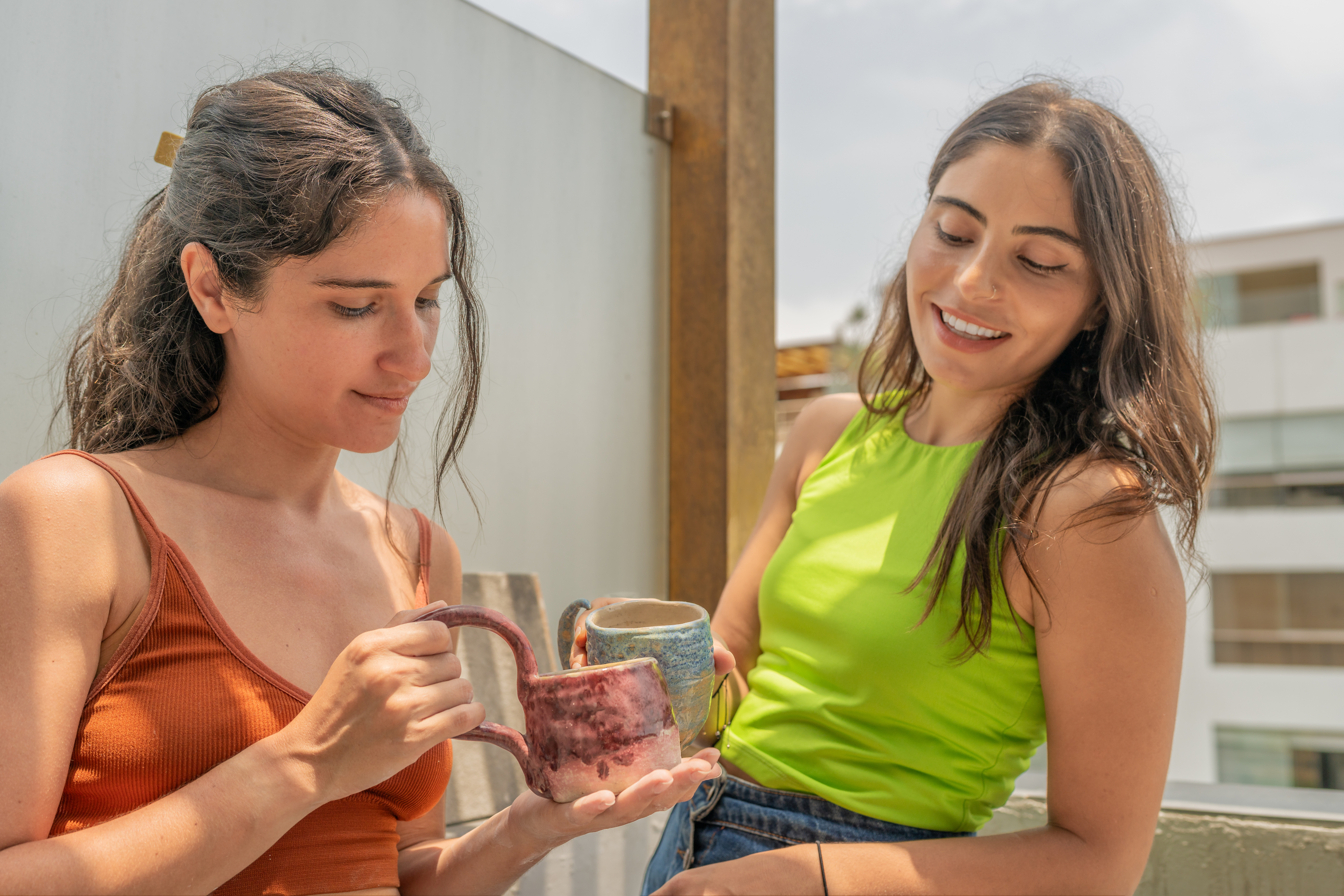 Two women smiling and holding ceramic mugs outdoors