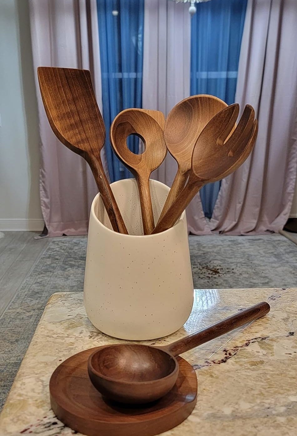 A set of wooden cooking utensils in a white holder with a wooden rest on a kitchen counter
