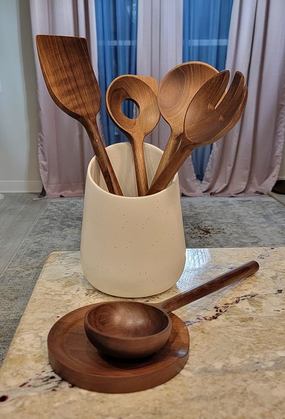 A set of wooden cooking utensils in a white holder with a wooden rest on a kitchen counter