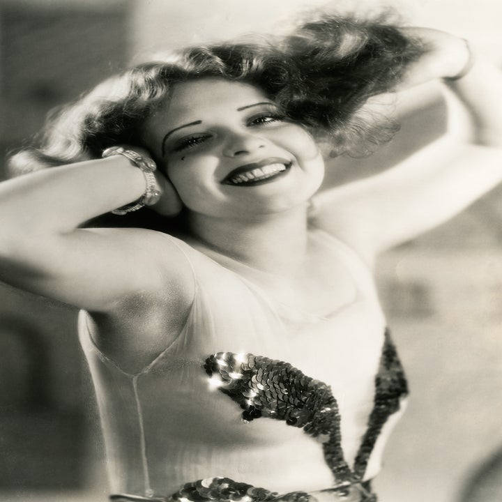 Vintage photo of a Clara Bow with a sequined dress, hands in hair, smiling broadly