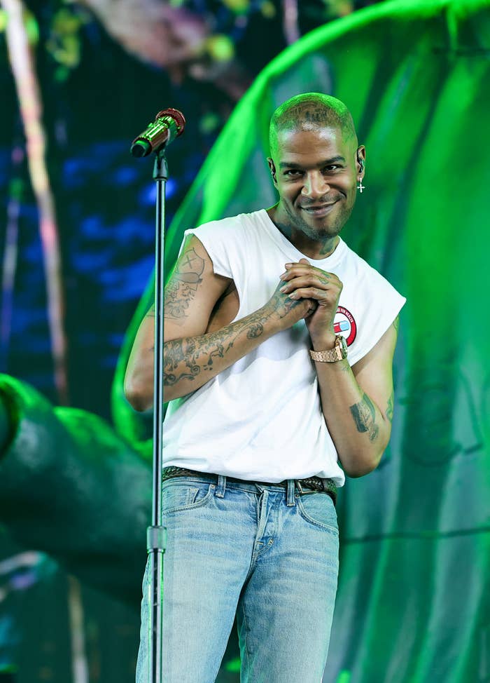 Kid Cudi onstage with his hands clasped as he smiles at the audience