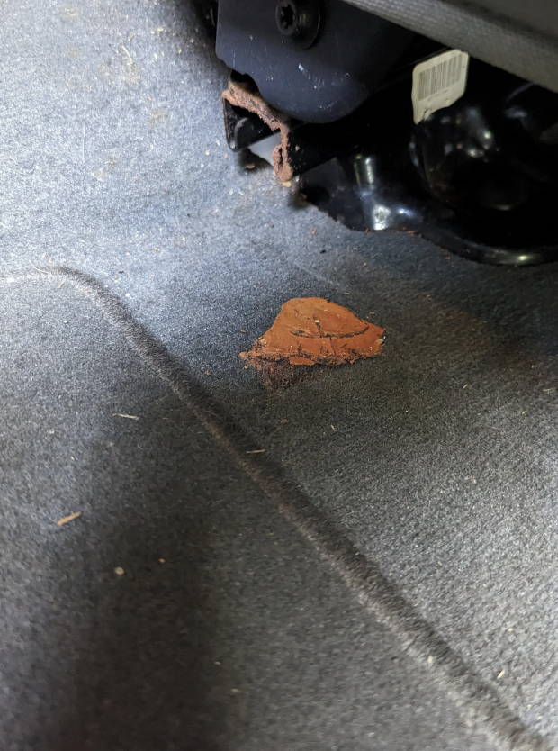 A close-up of a worn car floor mat with a brown stain