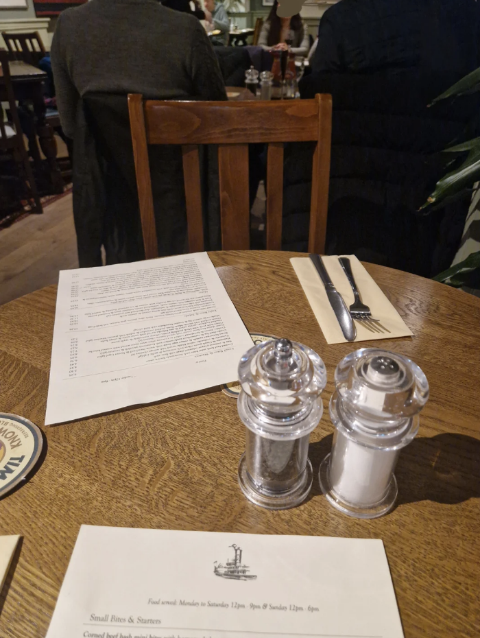 Restaurant table with menus, salt and pepper shakers, and people seated in the background