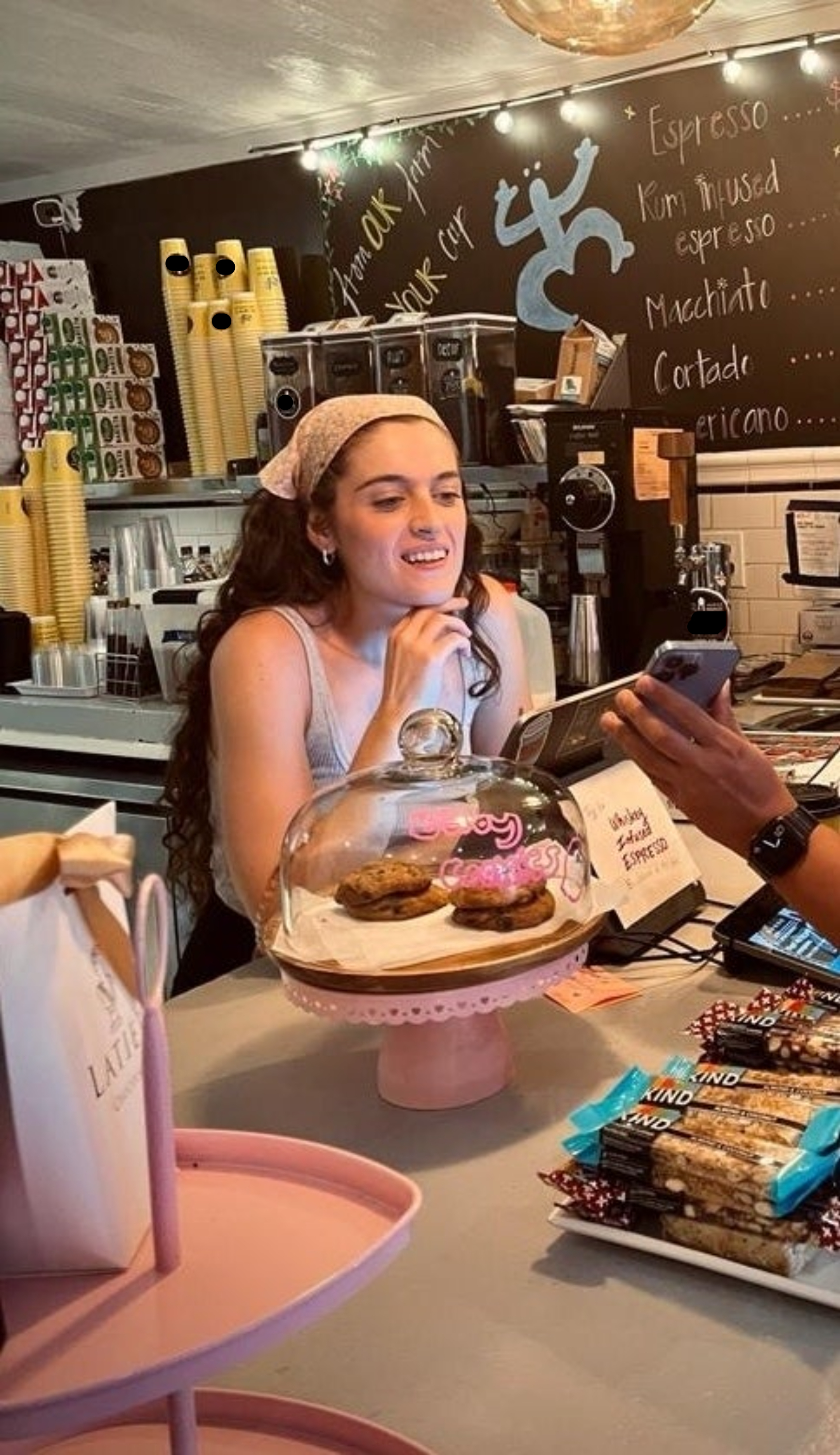 The author serving pastries at a coffee shop counter with a phone and menu board visible