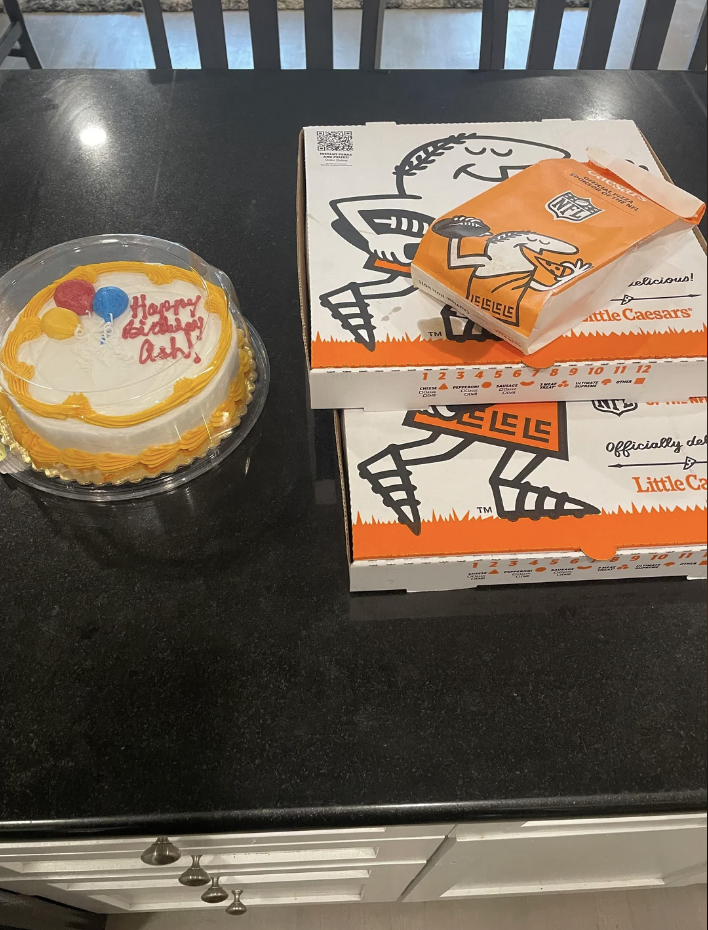 Birthday cake next to a Little Caesars pizza box on a kitchen counter