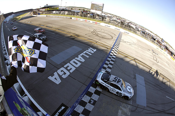 Race cars crossing the finish line with a checkered flag waving, skid marks on the track