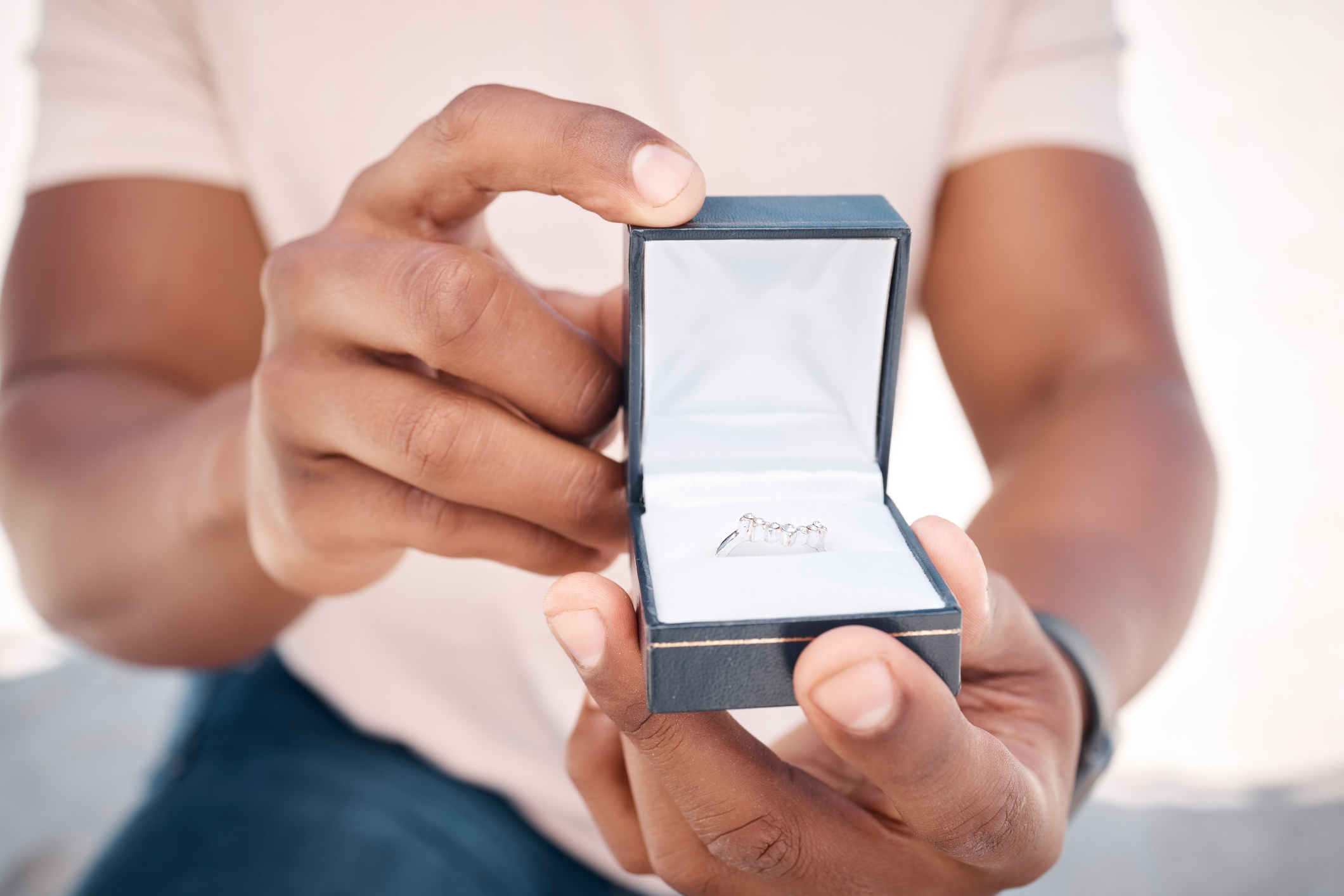 Person holding an open ring box with a ring inside, focus on the box, background blurred