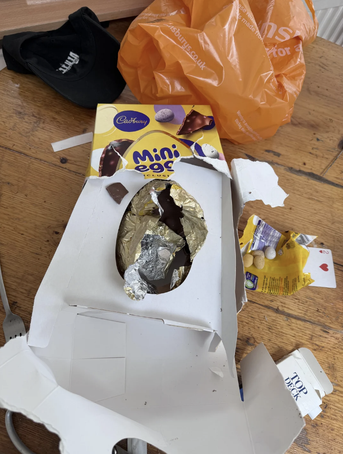 Opened Cadbury Mini Eggs packaging with a partially unwrapped chocolate egg and torn wrappers on a wooden surface