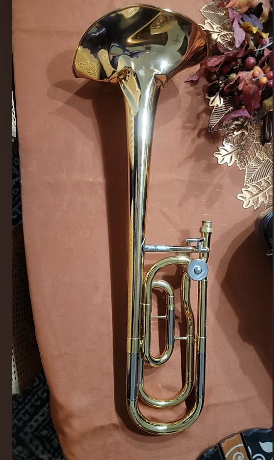 Shiny brass trombone standing vertically on a patterned surface with decorative foliage in background