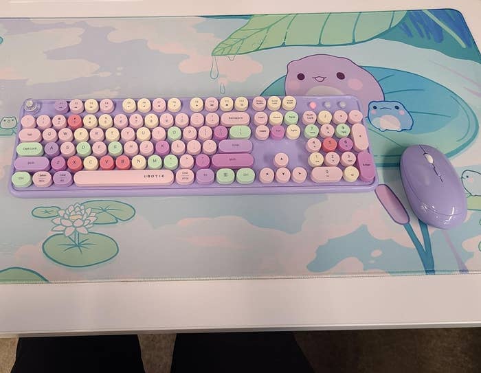 a reviewer photo of the lavender-themed keyboard and mouse on a whimsical animal print desk mat