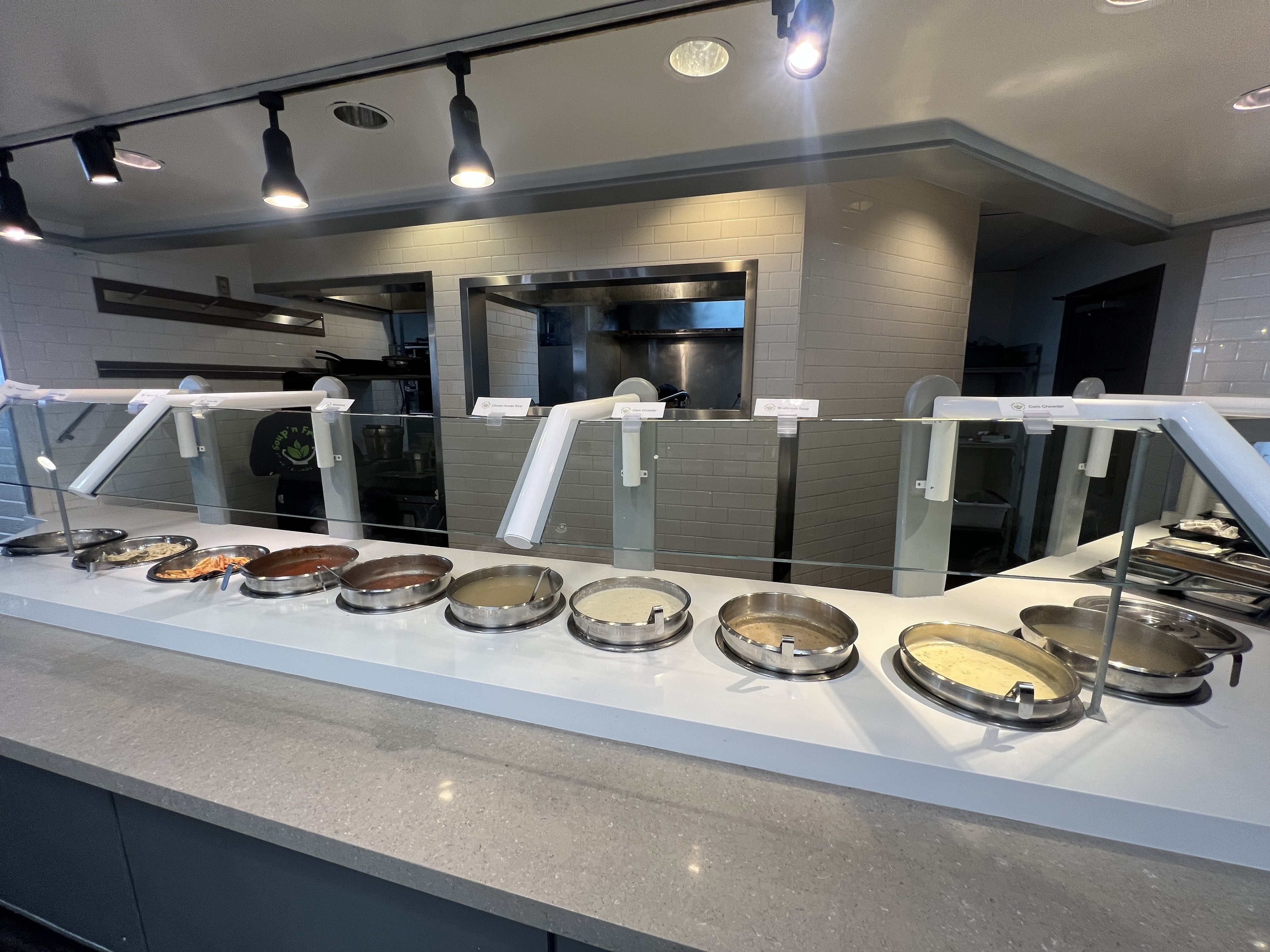A cafeteria counter with various trays of food behind a protective glass barrier