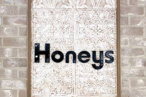 レンガ壁に取り付けられた装飾的な模様のあるドアに「Honeys」と書かれた看板が掲げられています。
