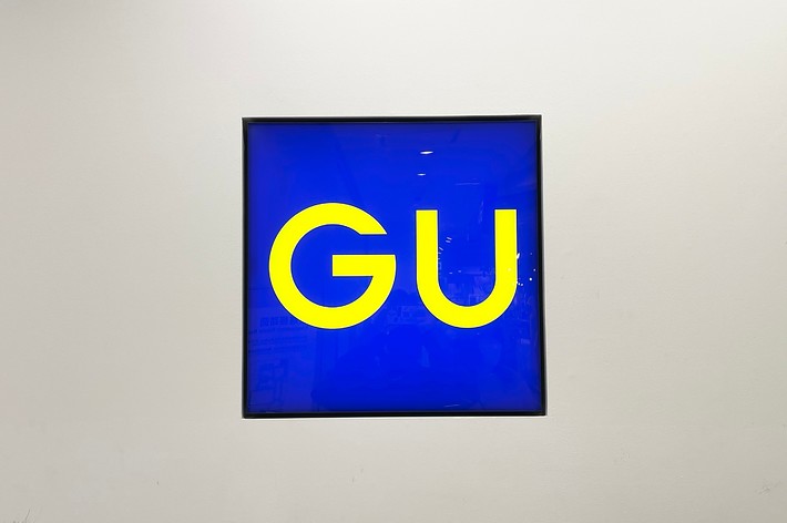 Artwork with the letters “GU” on a blue background, displayed in a simple frame on a white wall