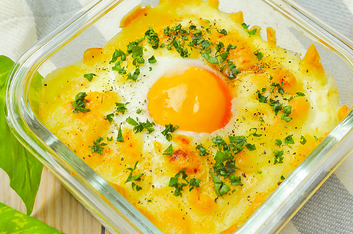 ガラス製の容器に入ったサニーサイドアップの卵、周りにチーズとパセリがトッピングされている。