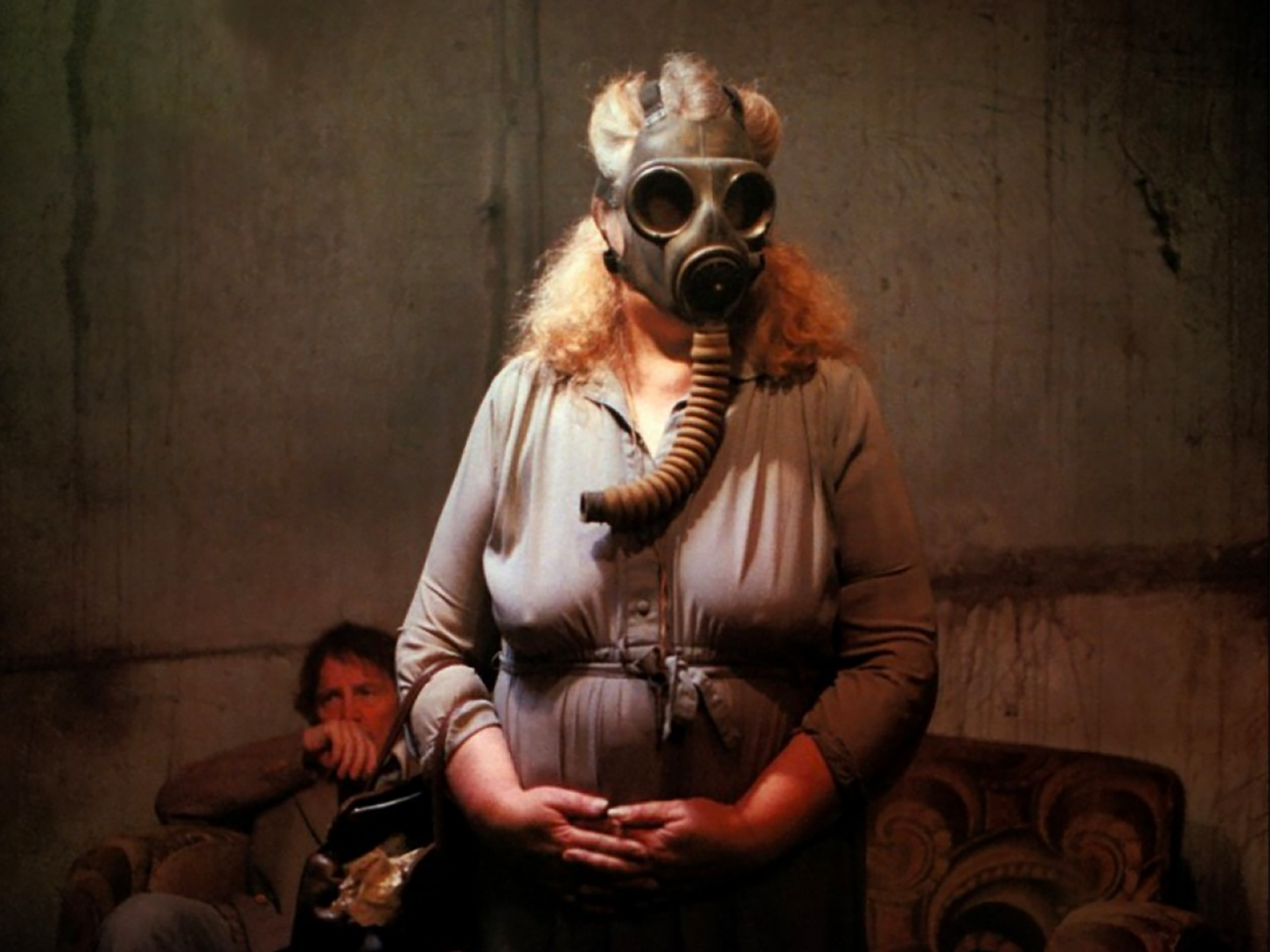 Two characters in a tense scene, one standing with a gas mask and one seated in the background