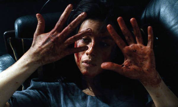 Woman with blood on hands and face looks distressed, in a dramatic movie scene