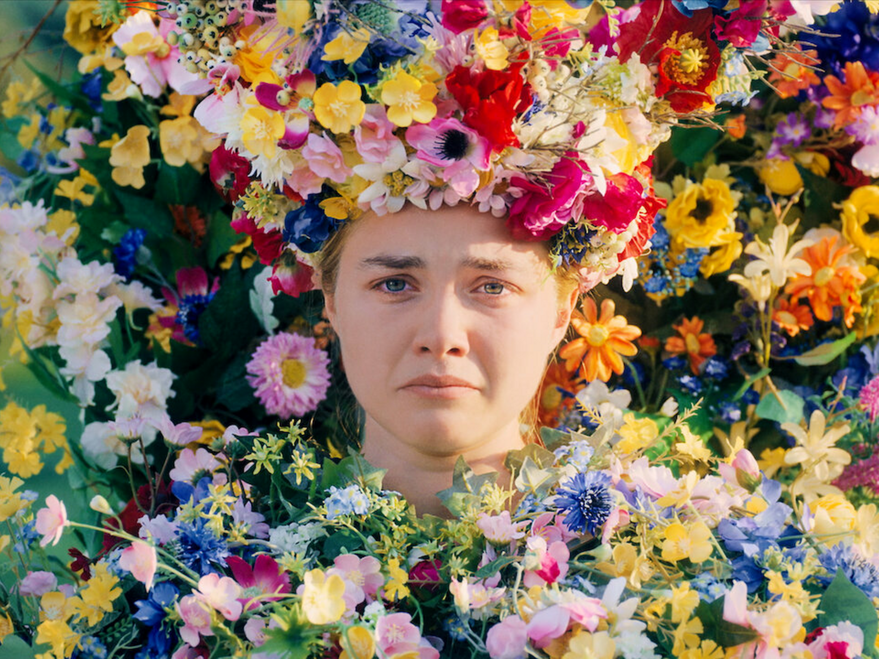 Person surrounded by assorted flowers with a large floral arrangement on their head. Expressing a solemn mood