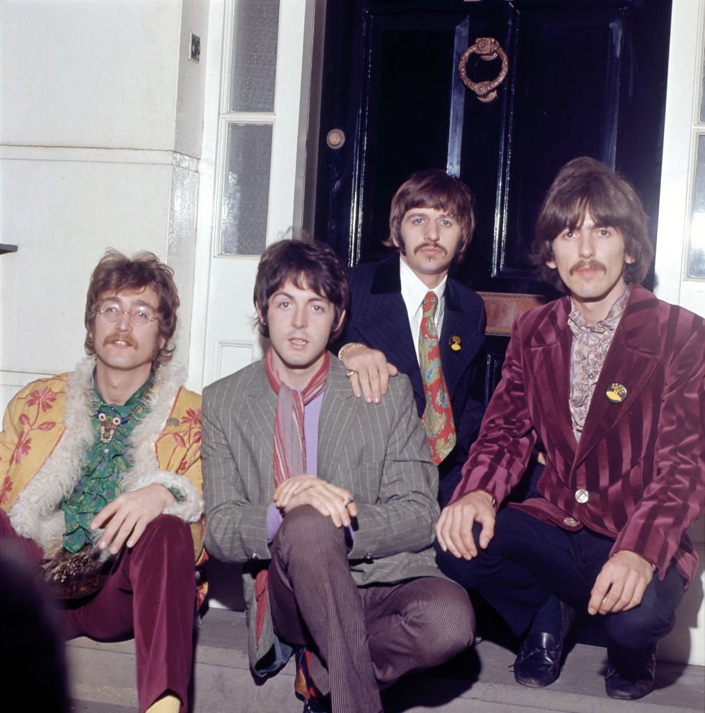 The Beatles posing together, wearing suits with flower patterns and ruffled shirts