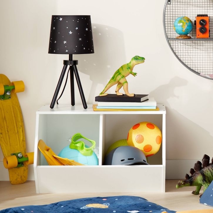 Shelving unit with various children&#x27;s items including a lamp, books, and toys, suggesting ideas for organizing a kid&#x27;s room