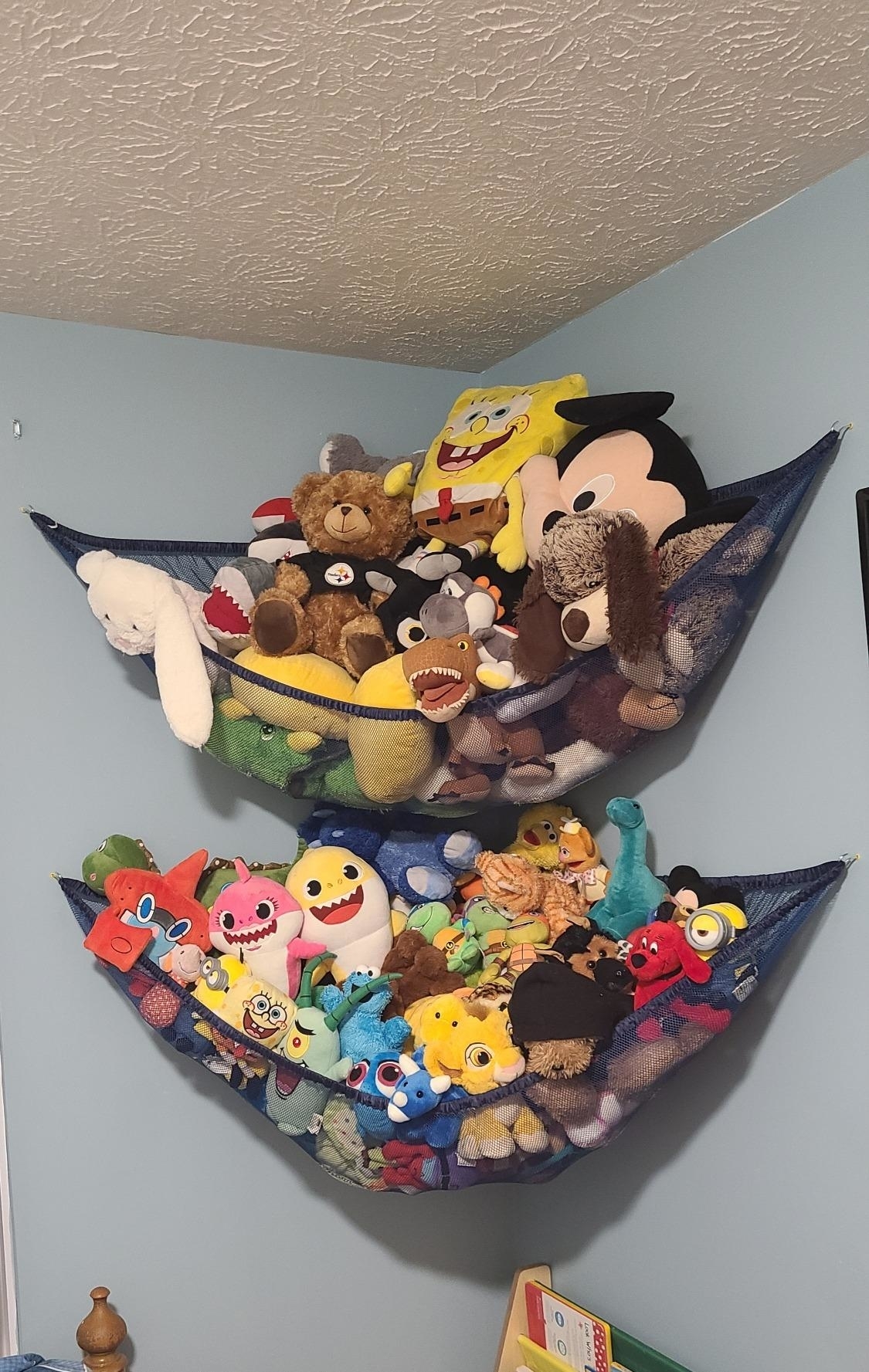Wall-mounted fabric storage pockets filled with assorted plush toys, including a SpongeBob and Mickey Mouse, ideal for organizing