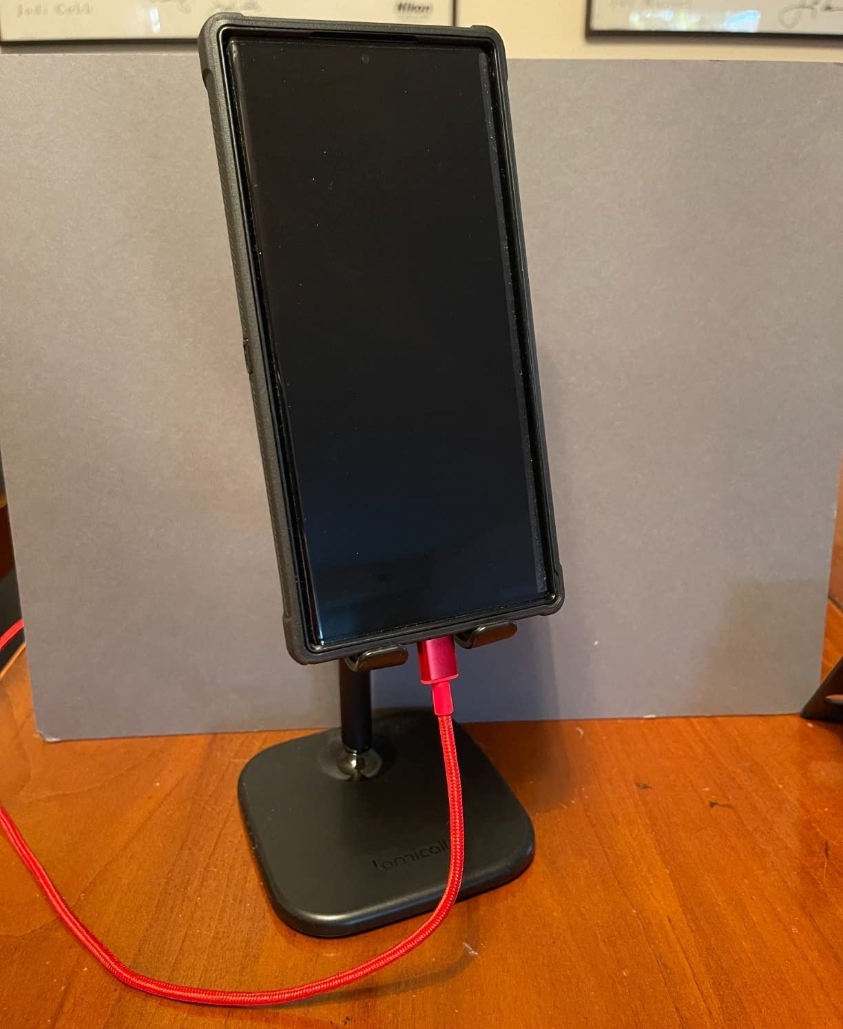 a reviewer photo of their smartphone mounted on a black stand with a red charging cable connected.
