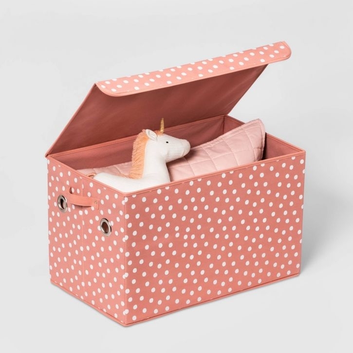 Polka-dotted storage box with a plush unicorn and pink cushion inside
