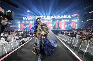 Wrestler in ornate robe with championship belt walks down ramp at WrestleMania event