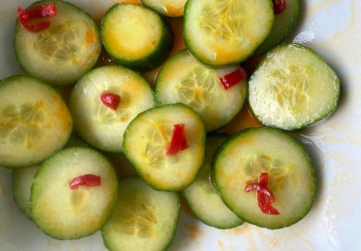 Sliced cucumbers with red chili pieces on top, displayed on a plate
