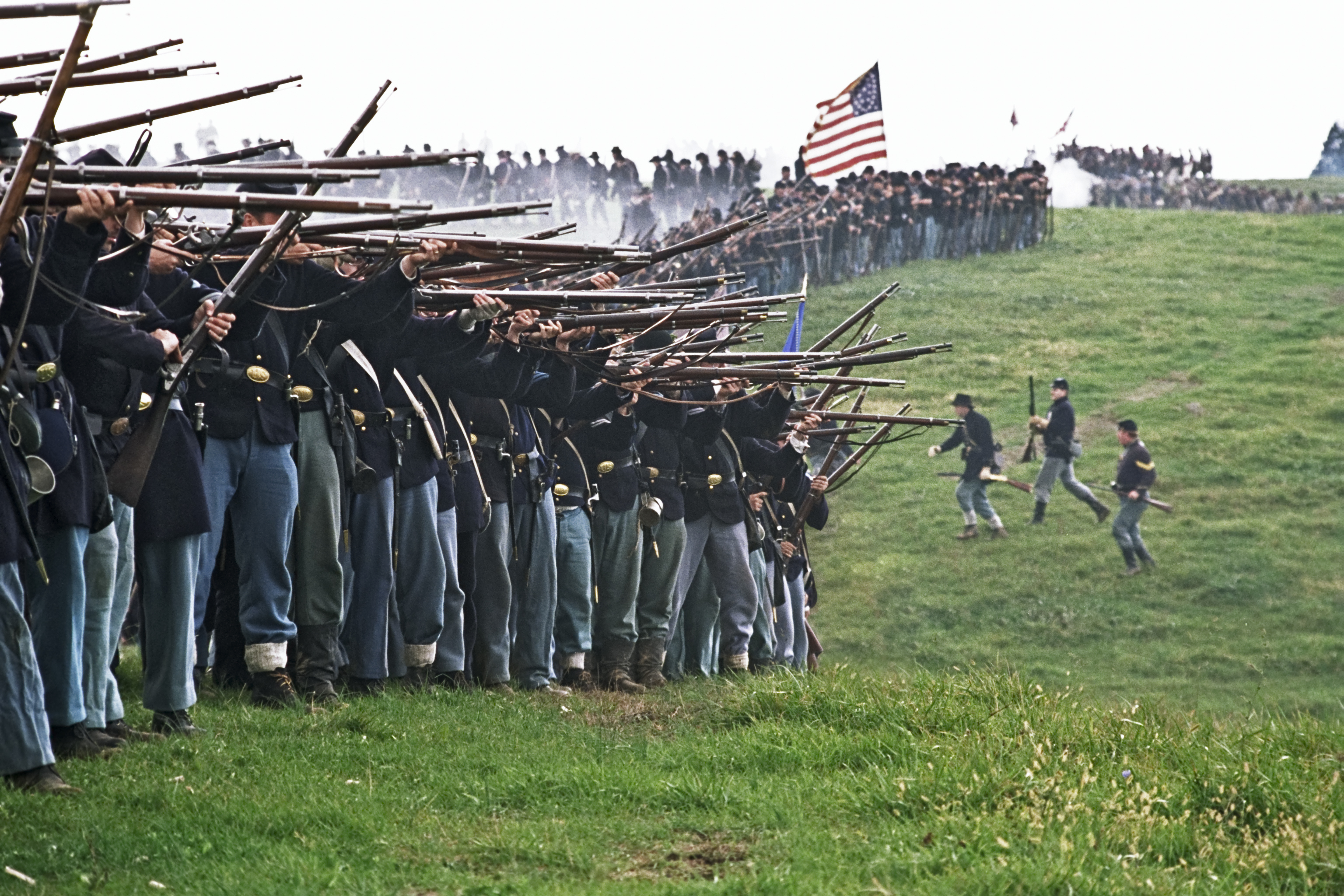 A reenactment of a historical battle with soldiers in uniforms holding rifles, carrying an American flag
