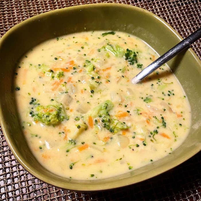 A bowl of creamy vegetable soup with broccoli, served on a woven placemat