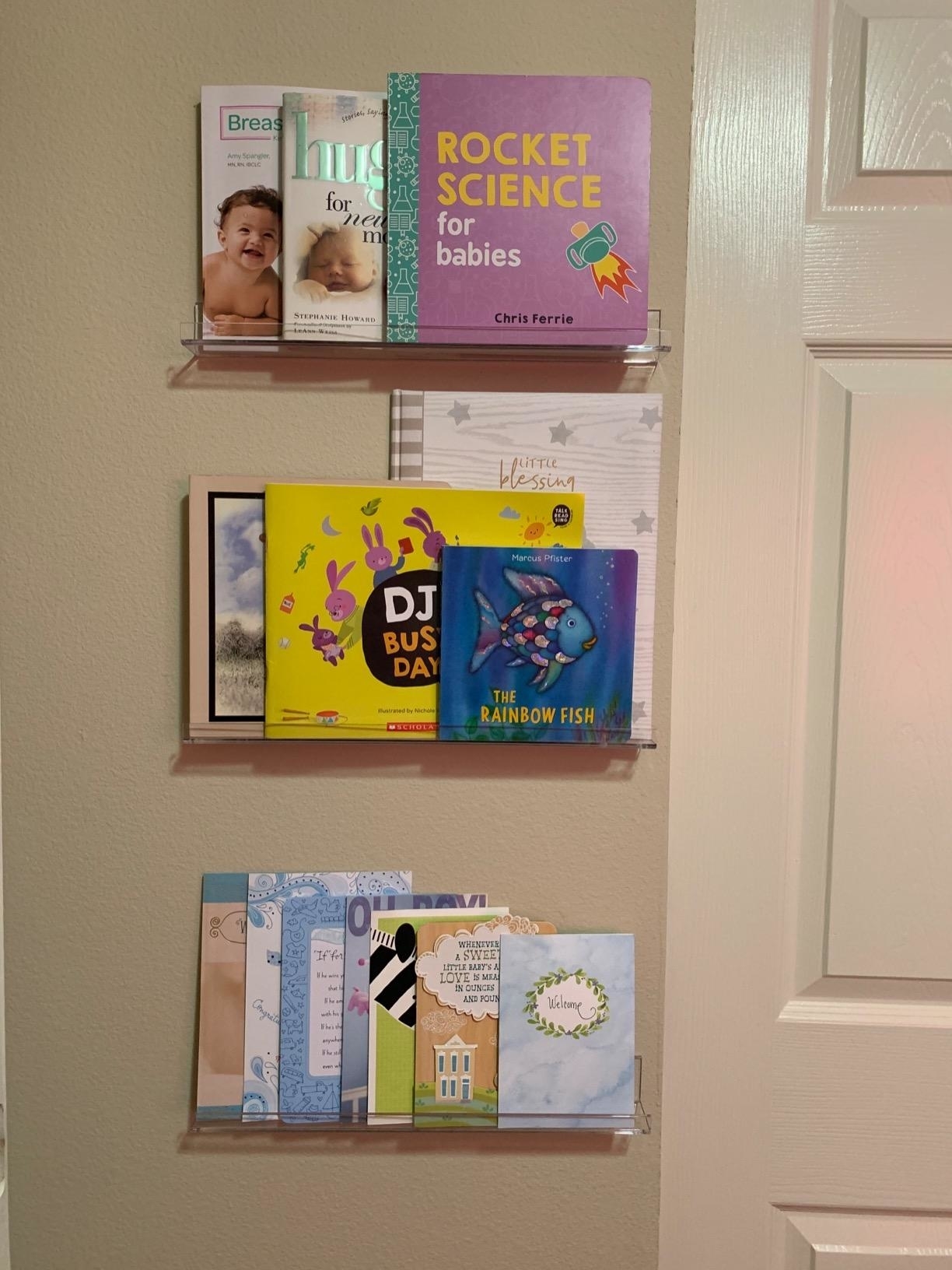 Acrylic wall shelves displaying a variety of children&#x27;s books and greeting cards, ideal for nursery organization