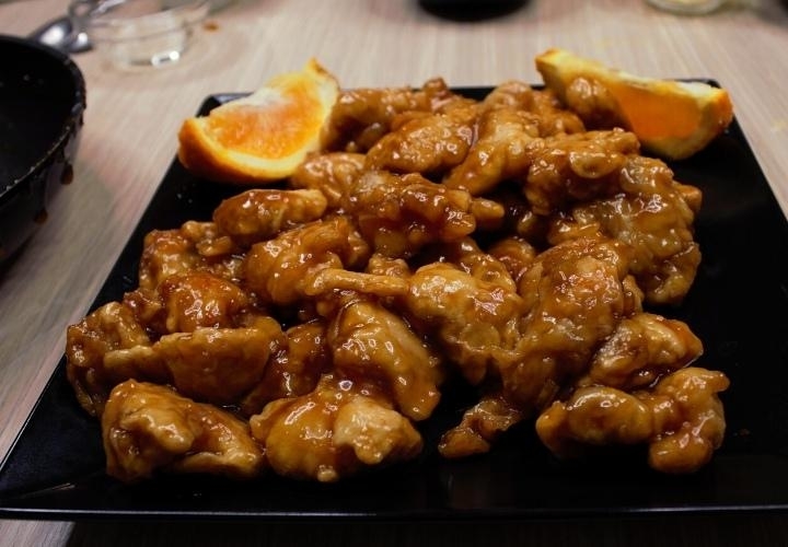 A plate of glazed chicken with orange slices on the side