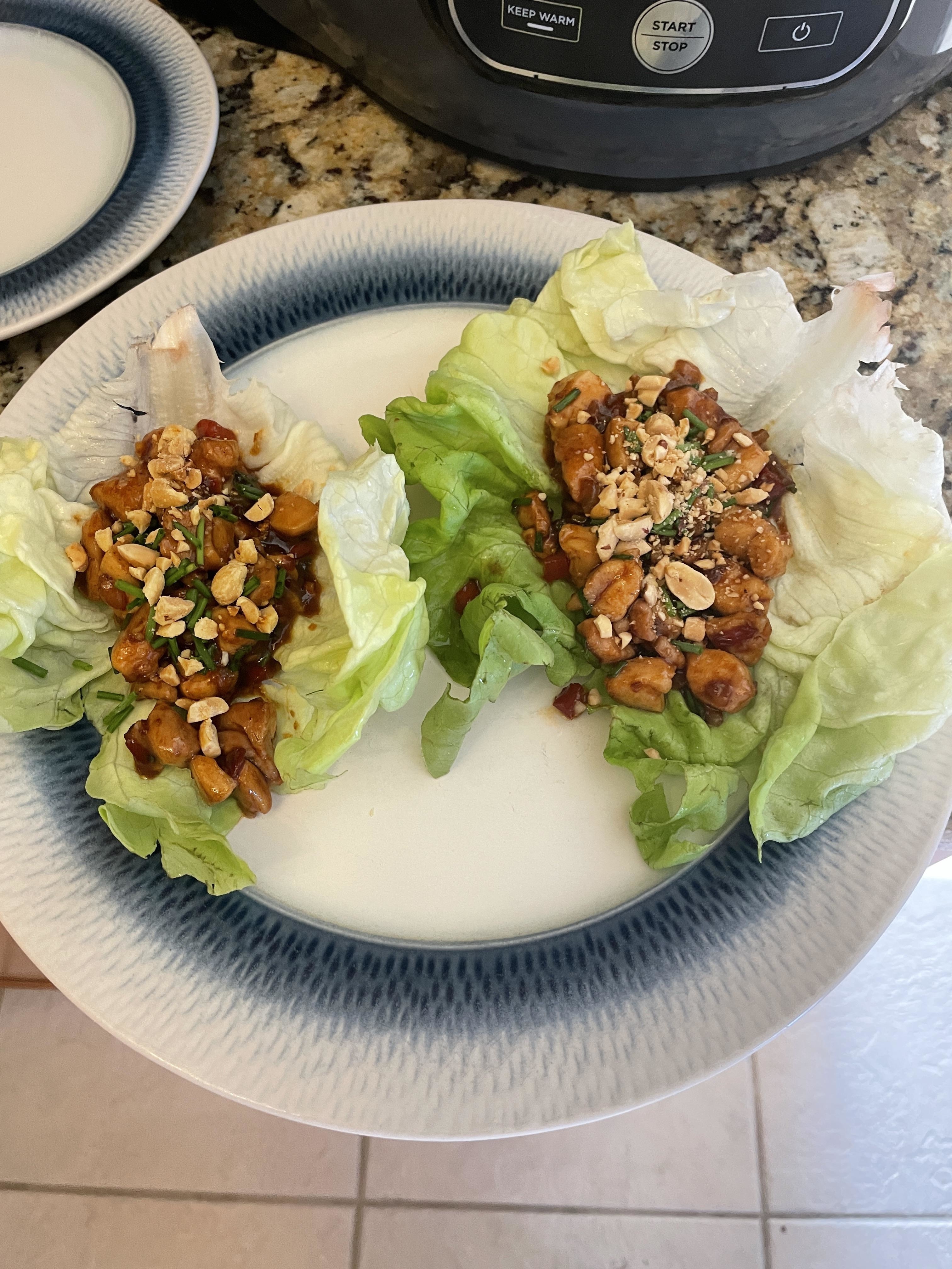 Two lettuce wraps filled with savory mix, topped with seeds on a plate