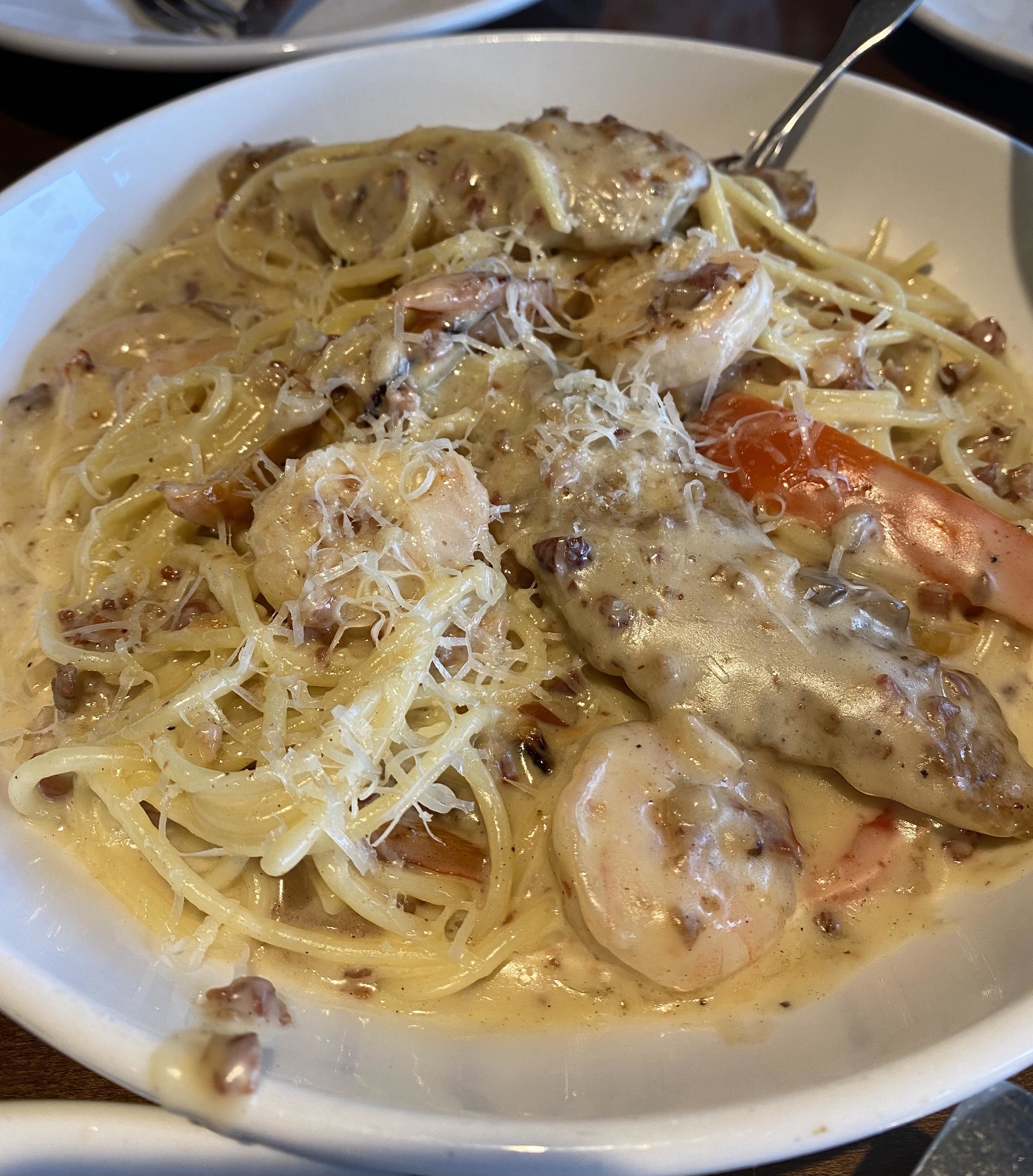 A plate of spaghetti with creamy sauce, chicken, shrimp, and sprinkled cheese