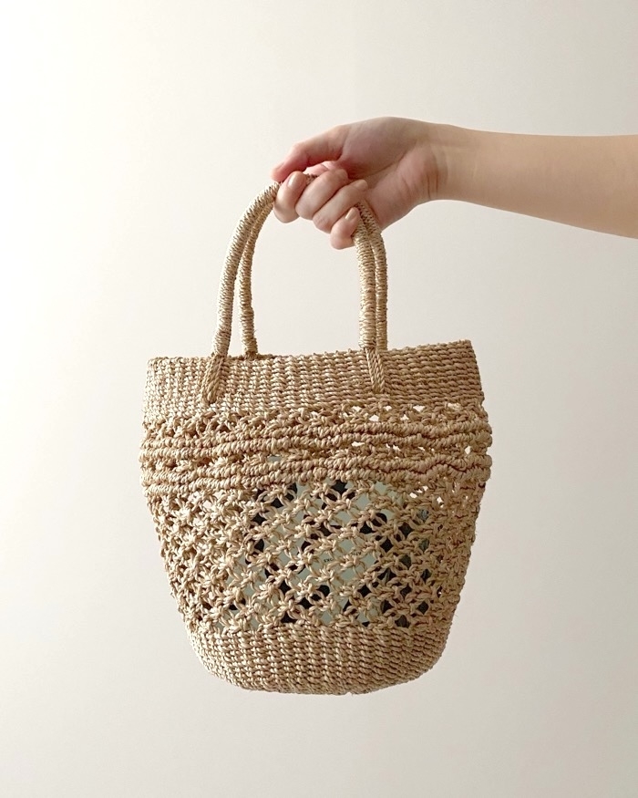 Hand holding a woven straw basket bag against a neutral background