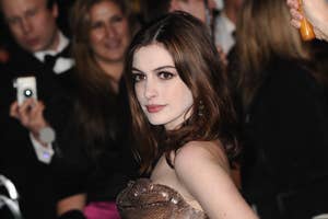Anne Hathaway in a shimmering strapless gown with a layered necklace, posing at an event
