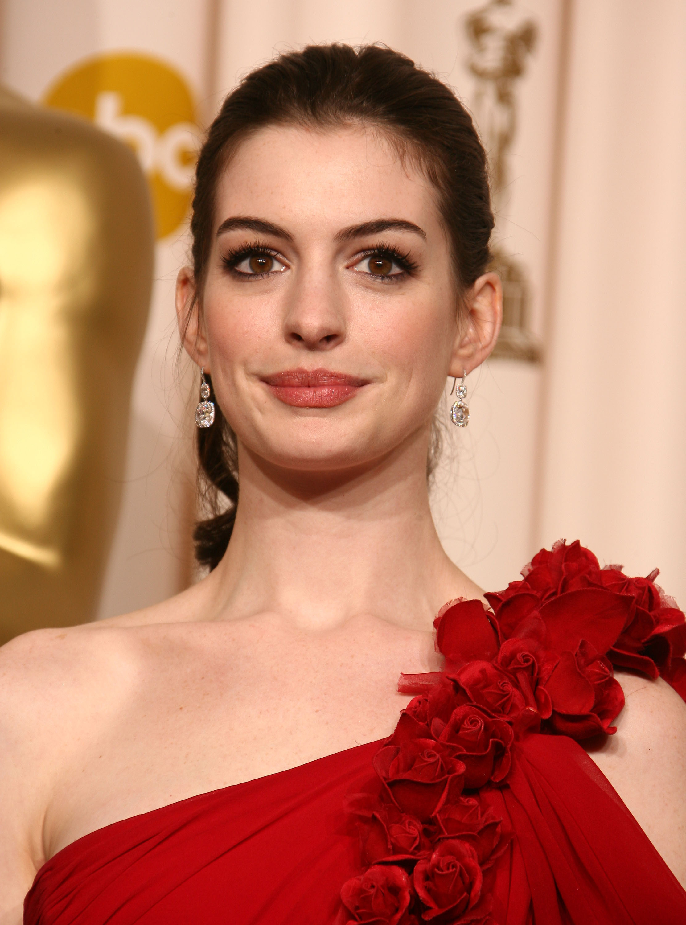 Anne Hathaway in a red gown with floral shoulder detail at an award event
