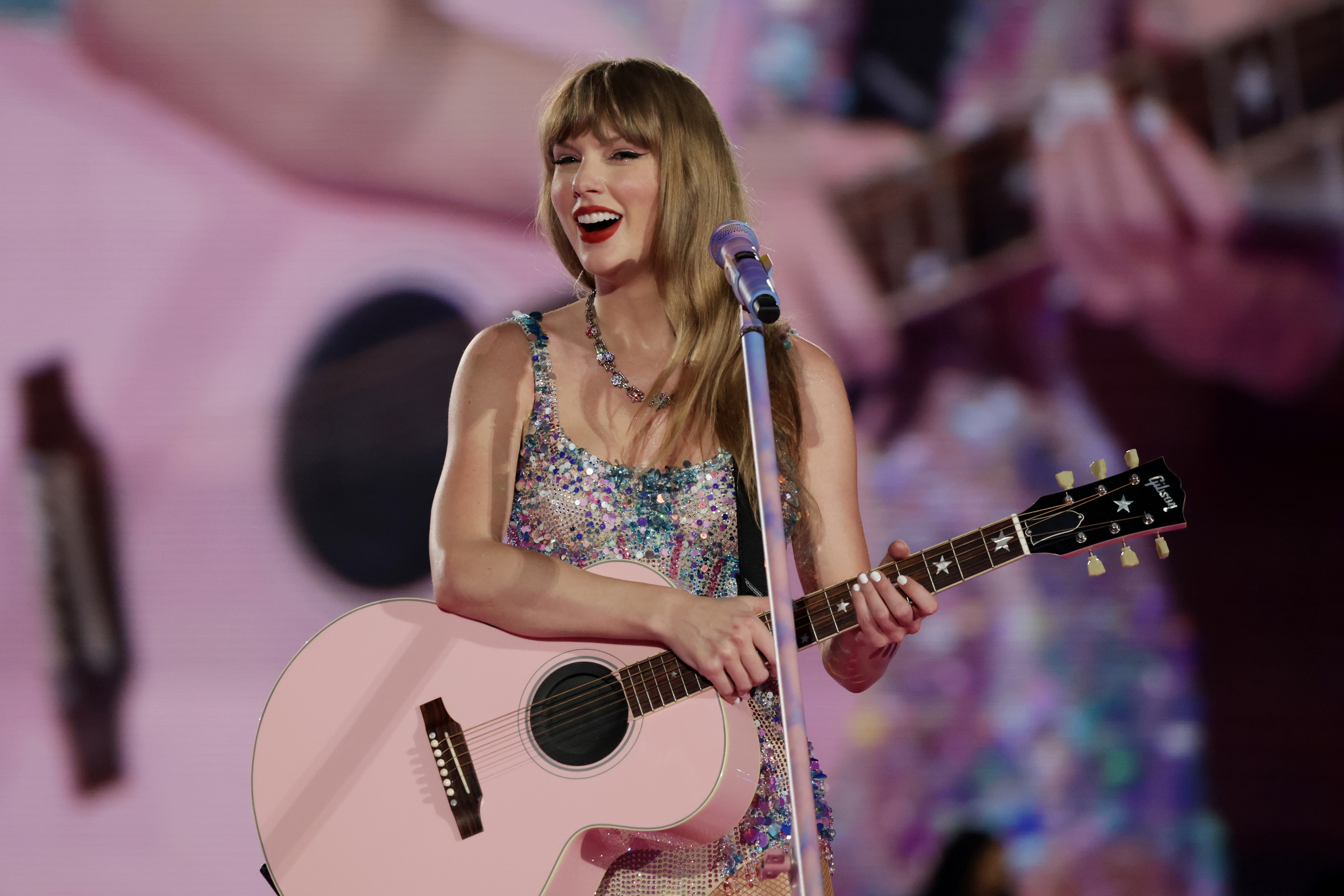 Taylor Swift performs on stage with a glittery top and a guitar