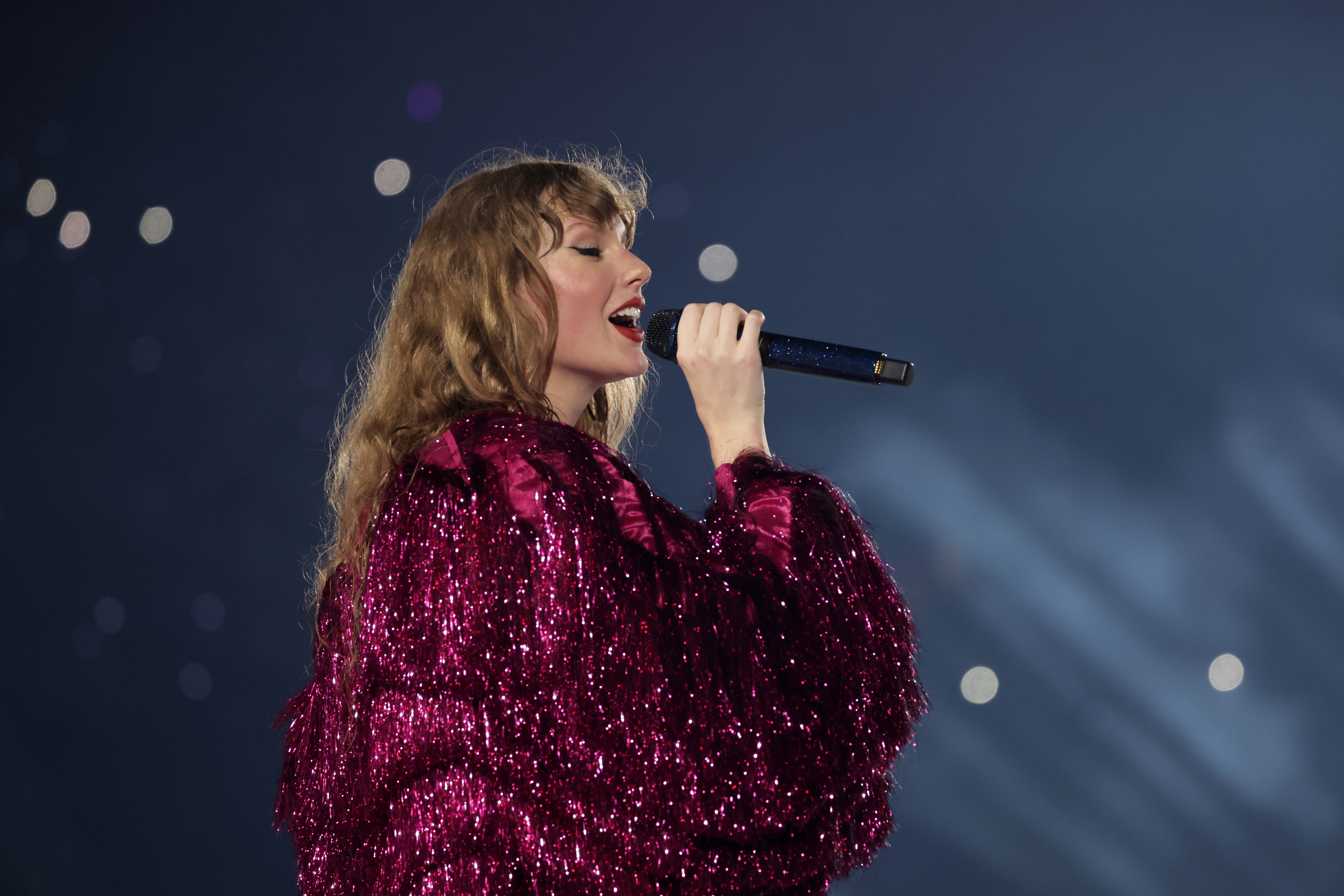 Taylor on stage singing into a microphone, wearing a sequined outfit