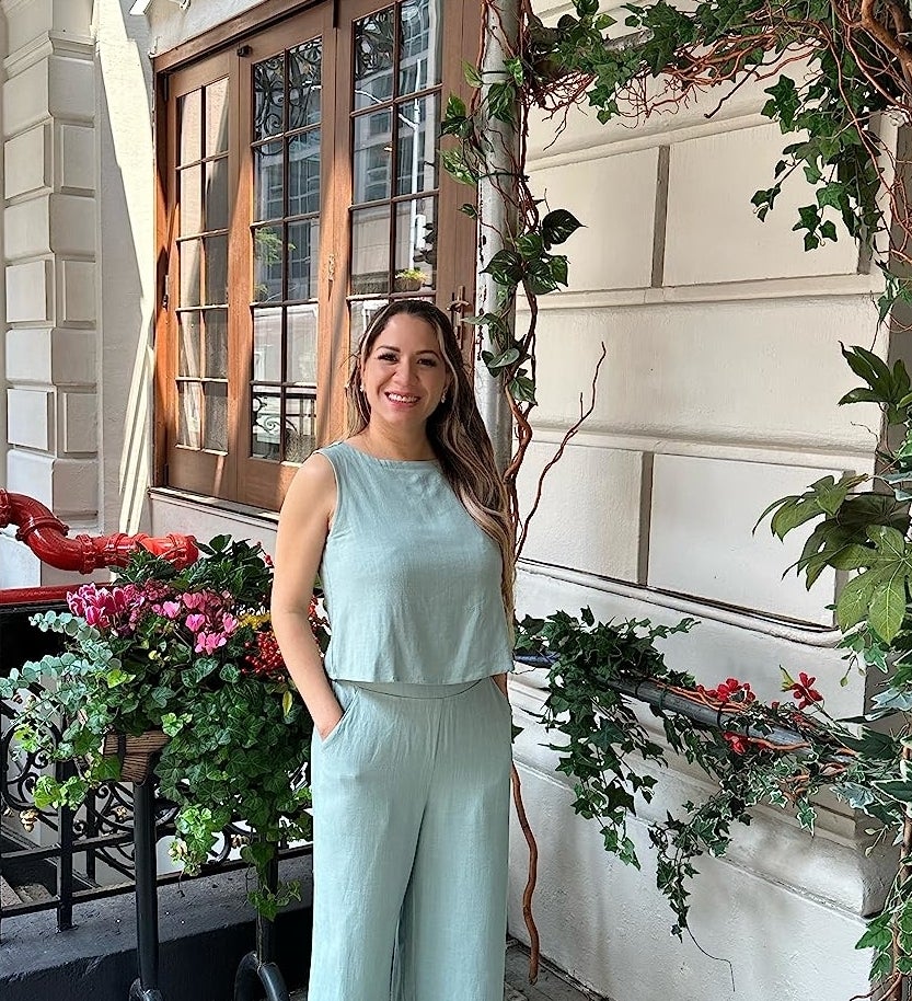 reviewer in a sleeveless jumpsuit posing by a flowered trellis outside a building