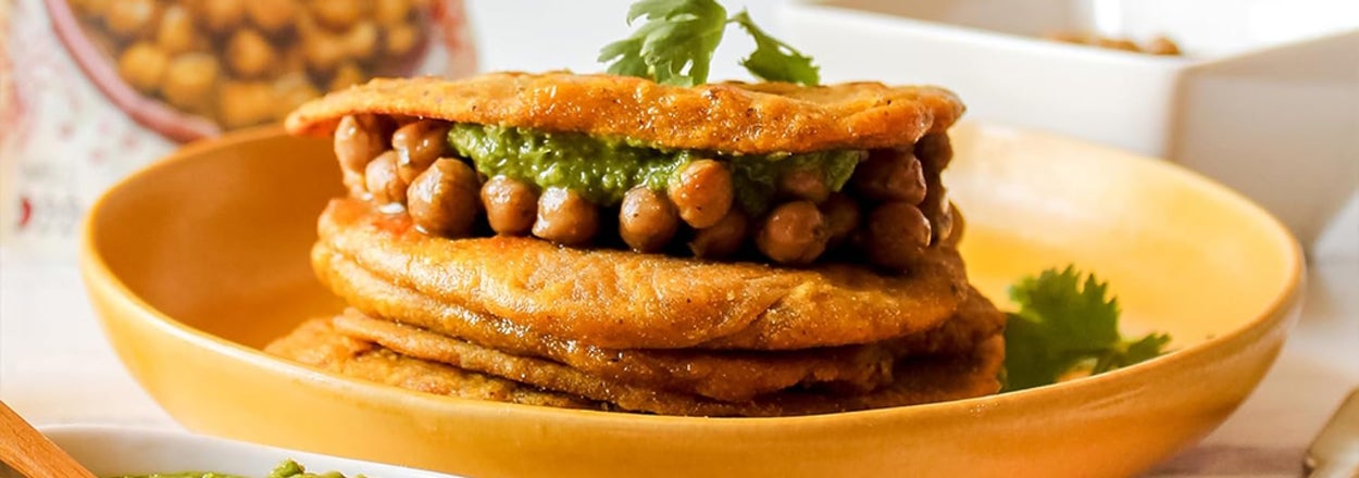 A stack of roti with chickpeas on top, next to a packet of A Dozen Cousins beans and a bowl of green sauce